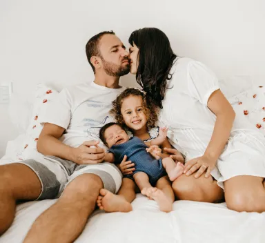 Man dna woman kissing on bed with two small children sitting between them