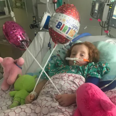 Girl in hospital bed with birthday balloons.