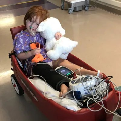 Girl with cast on her leg being pulled in wagon at hospital.