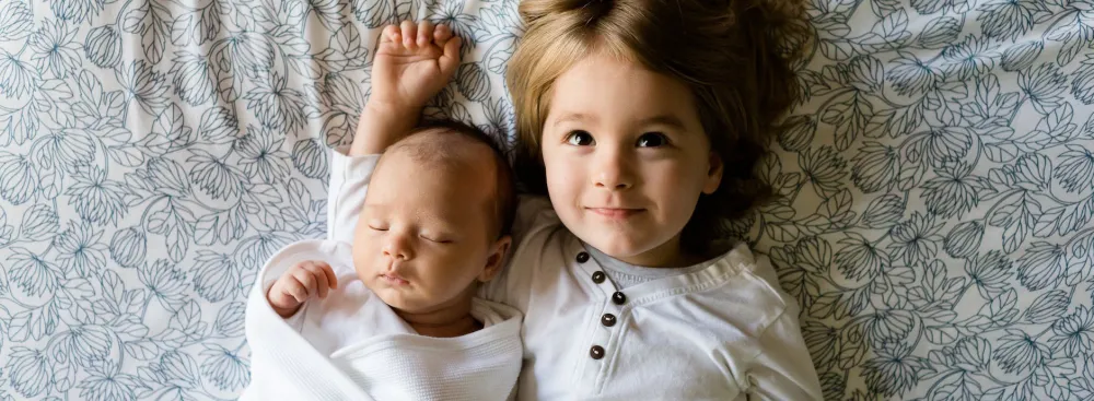 A small girl and an infant laying face up on the bed