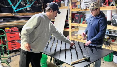 two men in a garage building hammering in short spokes to make to make a giant Plinko board 
