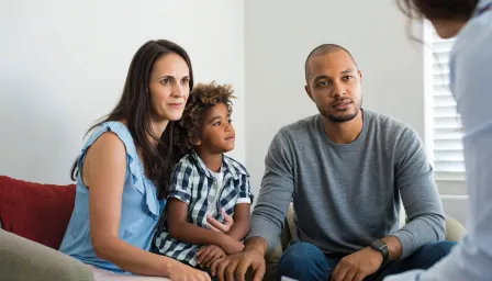 Parents with child on a couch listening to someone else speak