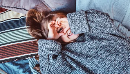 Young girl holding up her fingers in a heart shape over her eyes on a bed.