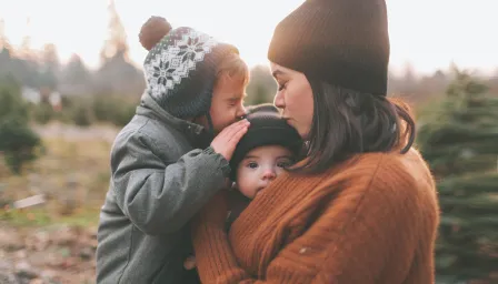 Woman outside holding two children and kissing one on the head