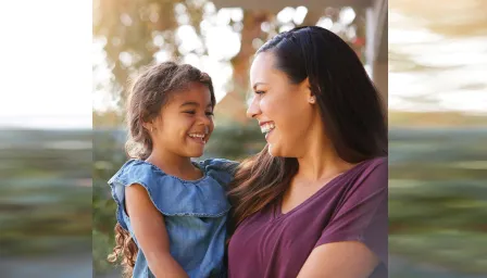 Mom holding her daughter outside smiling 